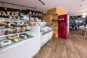Innenansicht einer Bäckerei mit Kuchendisplay, Getränkeautomat und Essbereich.