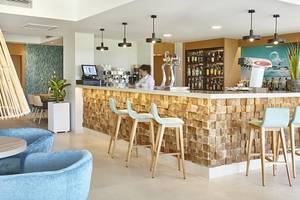 Innenbereich der Bar im Castell Royal Hotel mit Holztheke, blauen Stühlen und einer Angestellten.
