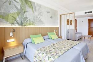 Schlafzimmer im Castell Royal Hotel mit zwei Betten, grünen Kissen und tropischem Wandbild.