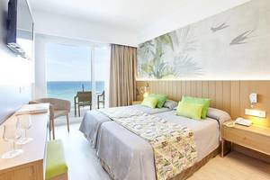 Zimmer im Castell Royal Hotel mit Blick auf das Meer, zwei Betten, grünen Kissen und einem Fernseher an der Wand.