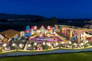 Außenbereich des Sandy Beach Hotel in Kos bei Nacht mit bunten Gebäuden und beleuchteten Spielgeräten.