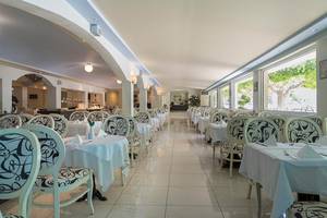 Restaurant im Sandy Beach Hotel auf Kos mit weißen Tischen und Stühlen und Glasfenstern.
