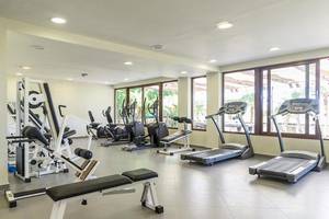 Fitnessstudio im Sandy Beach Hotel auf Kos mit verschiedenen Geräten und großen Fenstern.