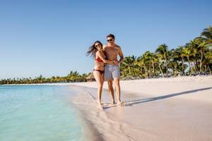 Ein Paar am Strand von Barcelo Maya Beach, umgeben von Palmen und klarem Wasser.