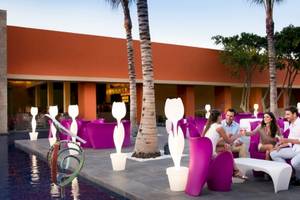 Vier Personen sitzen auf einem Außenbereich des Barcelo Maya Beach Hotels neben einem Pool.
