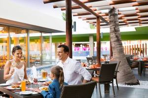 Familie sitzt am Tisch und genießt Essen im Barcelo Maya Beach Hotel Restaurant.