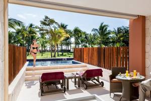 Ein Mann liest auf der Terrasse des Barcelo Maya Beach Hotels, neben einem Pool mit einer Frau in einem Bikini.