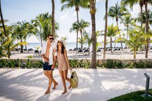 Ein Paar spaziert mit Einkaufstaschen am Barcelo Maya Beach Hotel am Strand.