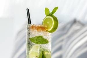 Ein Glas mit alkoholfreiem Cocktail, garniert mit Limetten und Minzblättern.