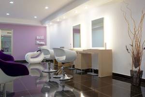 Friseursalon mit violetter Wand, weißen Stühlen und Spiegeln.