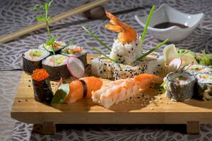 Ein Sushi-Platter mit verschiedenen Sushi-Rollen, Garnelen und Rettichscheiben auf einem Holzbrett.