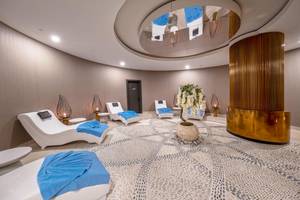 Innenbereich des Spa-Bereichs des Lago Hotels mit weißen Liegen und blauen Handtüchern.
