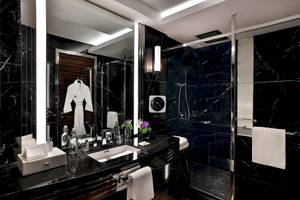 Luxuriöses Badezimmer im Marriott Resort Palm Jumeirah, Dubai, mit schwarzem Marmor, weißem Bademantel und frischen Blumen.