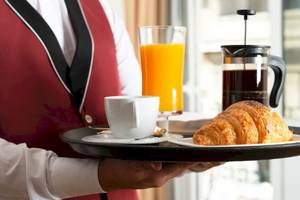 Ein Kellner serviert Frühstück mit Croissant, Kaffee und Orangensaft im Grand Palace Hotel.