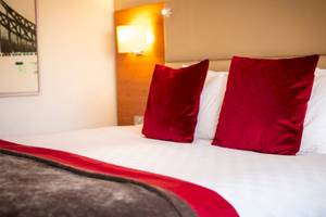 Hotelzimmer im Tower Hotel, London mit rotem Kissen, weißem Bettlaken und Decken, Lampen und Gemälde an der Wand.