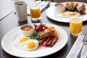Frühstück im Tower Hotel in London mit Spiegeleiern, Würstchen, Speck, Bohnen und Orangensaft.