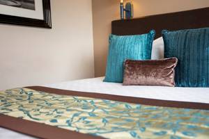 Das Bett im Tower Hotel London mit blauen und braunen Kissen und einer Wand dahinter.