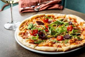 Eine Pizza mit Tomaten, Rucola und Oliven auf einem Holztisch im Tower Hotel, London.