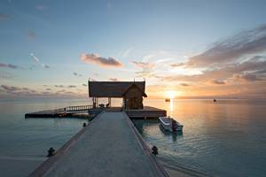 Sonnenuntergang über dem Constance Ephelia Hotel in Mahe, Seychellen, mit einer kleinen Hütte am Ende des Piers.