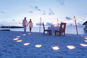 Ein Paar geht bei Nacht auf dem Strand, ein Tisch mit Kerzenlicht steht bereit, Constance Ephelia Mahe Seychelles