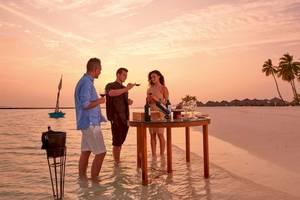 Drei Personen genießen Wein am Tisch auf dem Meer während des Sonnenuntergangs am Constance Ephelia Mahe Seychelles