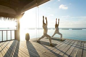 Zwei Personen praktizieren Yoga auf einer Holzplattform vor dem Meer.
