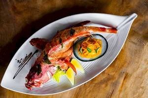 Ein gegrillter roter Fisch auf einem weißen Teller mit Beilagen
