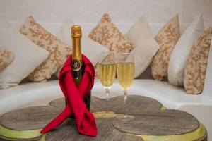 Eine Flasche Champagner mit zwei vollen Kelchen auf einem Tisch vor einem Sofa mit Kissen.