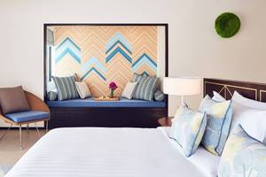 Hotelzimmer im Amari Havodda Maldives mit Bett, Sitzbank, Kissen und Lampe.