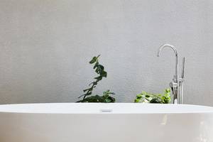 Weiße Badewanne im Badezimmer des Amari Havodda Hotels mit einem Hahn und Pflanzen im Hintergrund.