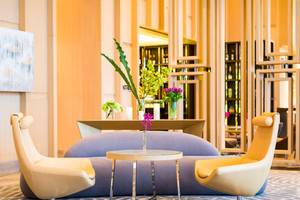 Lobby des AVANI+ Riverside Bangkok mit Sofas, Tisch, Blumen und moderner Einrichtung.