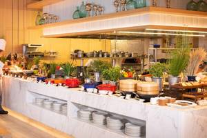 Restaurant im AVANI+ Riverside Bangkok mit Buffet und Köchen, die Speisen zubereiten.