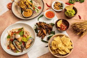Essen und Beilagen von Novotel Bangkok Sukhumvit 20, einschließlich Salat, Dips, Tortilla-Chips und Getränke.