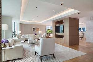 Wohnzimmer im Siam Kempinski Hotel Bangkok mit weißen Möbeln, Holzboden und zentralem Fernseher.
