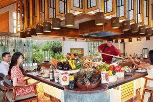 Menschen sitzen an einem Buffettisch im Amari Havodda Maldives Hotel und essen mit einem Koch.
