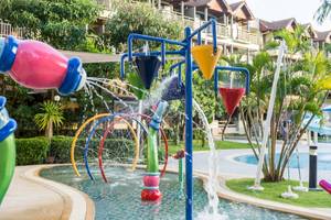 Wasserspielplatz des Phuket Marriott Resort & Spa am Merlin Beach mit bunten Wassersprudlern und Gebäuden im Hintergrund.