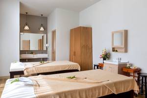 Spa-Behandlungsraum im X10 Khaolak Resort mit zwei Massagetischen, Waschbecken und Dekoblumen.