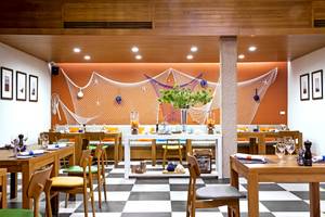 Innenraum des X10 Khaolak Resorts mit oranger Wand, weißen Netzen, schwarzen und weißen Schachbrettboden und mehreren Holztischen.