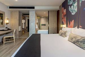Innenansicht eines Hotelzimmers im La Flora Khao Lak, mit einem Bett, Schreibtisch und Badezimmer.