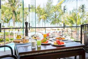 Frühstückstisch im The Haven Khao Lak mit Blick auf den Pool und Palmen.