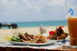 Tisch am Strand mit Essen und Getraenke, Hintergrund zeigt Meer und Himmel