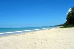 Eine breite, helle Strandfläche mit blauem Himmel und ruhigem Ozean im Hintergrund.
