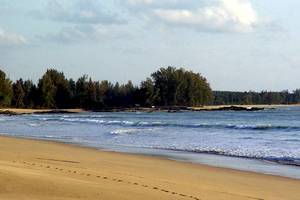 Strand von Bangsak Village mit blauem Wasser und grünen Bäumen im Hintergrund.