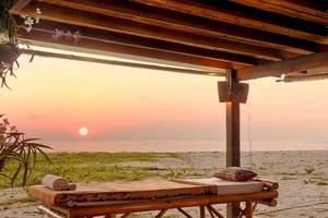 Zwei Massagebetten auf dem Strand unter einem Dach während des Sonnenuntergangs.