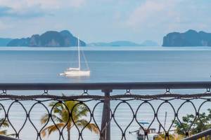 Aussicht auf das Meer von den TreeHouse Villas Koh Yao mit einem Boot und Bergen im Hintergrund.