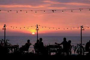 Menschen sitzen bei Sonnenuntergang am Meer auf einem Tisch im Freien des Haadson Resorts.