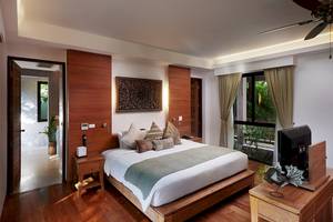 Innenansicht eines Schlafzimmers im Khaolak Paradise Resort mit großem Bett, Holzmöbeln und einem Fernseher auf einem Nachttisch.