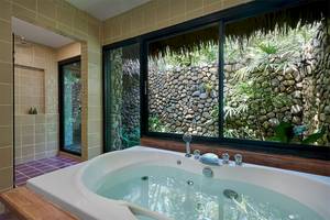 Badezimmer im Khaolak Paradise Resort mit Badewanne und Fenster mit Blick auf einen steinernen Garten.