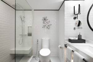 Modernes Badezimmer des Meliá Koh Samui Hotels mit weißen Fliesen und einer Glasdusche.
