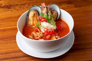 Ein weißer Porzellanschale mit Thai-Suppe, die mit Garnelen, Muscheln und roten Chilis garniert ist.